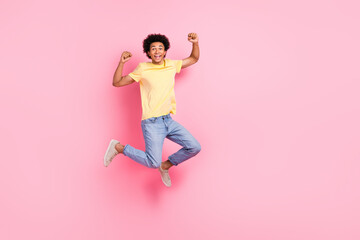 Full length portrait of nice young man jump raise fists empty space wear yellow t-shirt isolated on pink color background