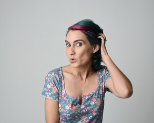 a close up head and shoulders portrait of young alternative female model, with pink and grey shaved undercut hair style, wearing a floral blue top. dramatically pulling expressive facial expressions. 