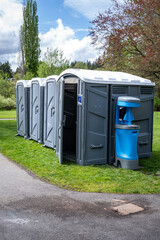 Setting up for a spring festival in a grass field in the park, portable bathrooms, including wheelchair accessible option, with a handwashing and sanitation station, sunny day outside
