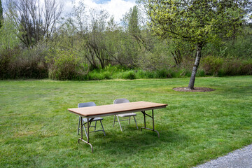 Obraz premium Setting up for a spring festival in a grass field in the park, temporary folding table and two chairs for participant sign in 
