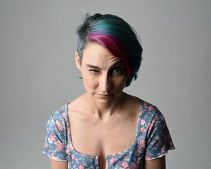 a close up head and shoulders portrait of young alternative female model, with pink and grey shaved undercut hair style, wearing a floral blue top. dramatically pulling expressive facial expressions. 