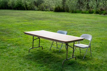 Setting up for a spring festival in a grass field in the park, temporary folding table and two chairs for participant sign in
