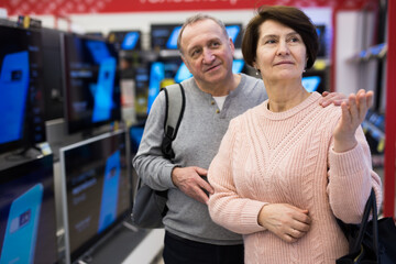 Middle aged man and woman choosing TV while shopping in electronic store.