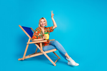 Photo of cheerful glad funky girl wear stylish print clothes vacation party v-sign isolated on blue...