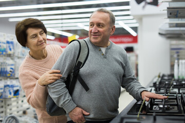 Happy spouses of mature age, who came to the electronics and home appliances store, choose a gas...