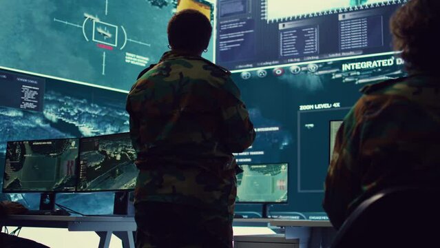 Female brigadier general gather intelligence reports on a big screen, ensuring national safety. Overseeing planning and coordination for a special mission, military reconnaissance system. Camera B.