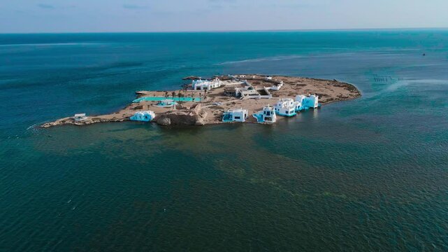 An aerial view of el biben island with a pool and hosting houses sits in the middle of the ocean with palm trees on it, surrounded by water creating a beautiful atmosphere. from Zarzis at Tunisia