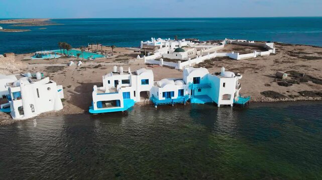 An aerial view of el biben island with a pool and hosting houses sits in the middle of the ocean with palm trees on it, surrounded by water creating a beautiful atmosphere. from Zarzis at Tunisia