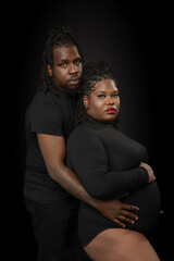 A serious studio profile portrait of a beautiful African-American couple posing for maternity portraits