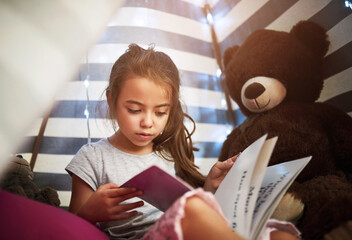 Learning, kid and reading book in home tent for education, language development or knowledge in bedroom. Girl child, fairytale or studying fantasy story, information or hobby with teddy bear in house © Lyndon/peopleimages.com