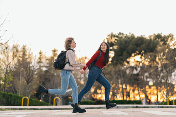 Fototapeta premium two student girls crossing crosswalk holding her hands, running and smiling