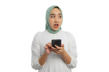 Shocked young Asian woman in green hijab and white blouse holding smartphone and looking aside at copy space, showing amazed expression isolated on white background