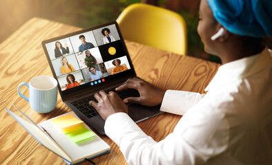 Black woman uses her laptop to engage in a virtual business meeting with multiple colleagues. She...
