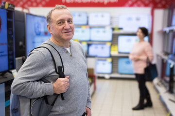 European mature man standing in televisions department in appliance store and looking at camera.