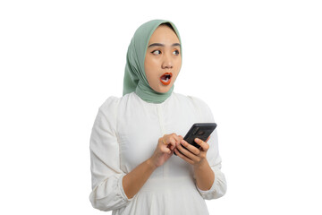 Shocked young Asian woman in green hijab and white blouse holding smartphone and looking aside at copy space, showing amazed expression isolated on white background