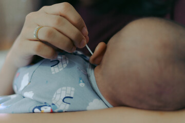 A mother hand cleaning her daughter's ear using cotton bud