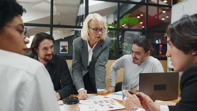 Diverse co-workers in office, creative designers discussing and making decisions. Team of multinational professionals looking at laptop display, talking about business idea and sales reports, teamwork