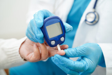 Asian doctor using digital glucose meter for check sample blood sugar level to treatment diabetes.