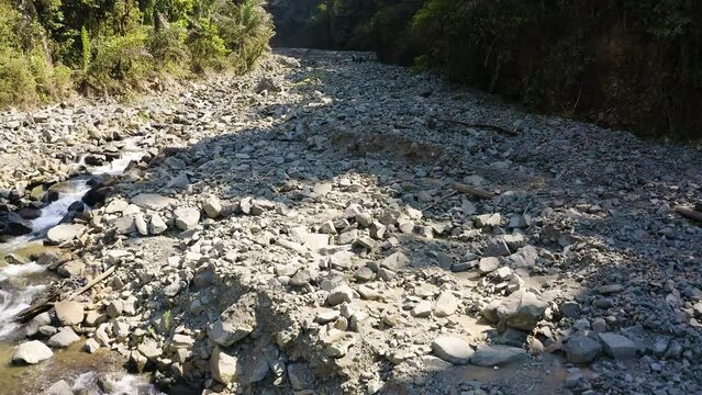 Aerial footage dolly in of unrecognizable people with backpacks walking on unstable rocky terrain next to a small river 60fps 2.7K