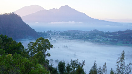 Fog on mountains scenery at sunrise with soft and warm morning light. Natural nature landscape background. Kintamani, Bali.