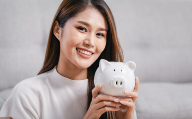 Young Asian woman with white piggy bank, Indoors.