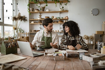 Bearded mature man and woman creating pottery while recording online course or content for blog. Man sculpting vase, woman sculpting plate. Collaborative creative process captured in studio.