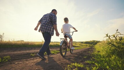 Fatherhood and childhood, dad teaching son riding bicycle in summer weekend. Happy joint time of family, single father and child resting in countryside in vacation, slow motion, rear following shot