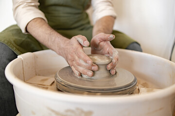 Adult male potter engages in the art of sculpting a ceramic dish using a potter's wheel, showcasing skill and precision.