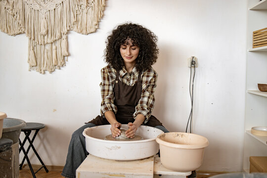 Young female potter creating ceramic bowl at pottery wheel in art studio. Focused on craftsmanship and creativity. - Powered by Adobe
