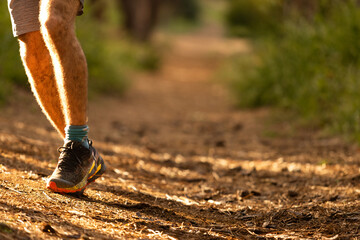 A man with hairy legs is wearing black shoes and is walking on a dirt path