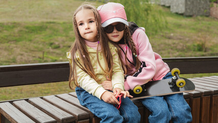 Close-up shot of two little girls sitting with their skateboards near a park and talking.