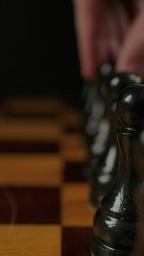 Human's hand makes first opponent move by black pawn e7 e5 in chess game. Macro parallel dolly shot of wooden authentic chess. Two players gaming. Vertical shot.