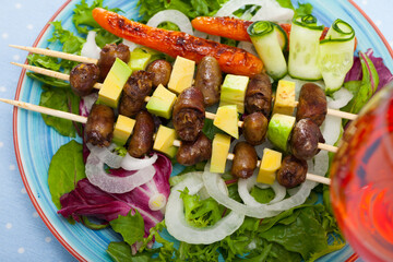 Delicious fried shish kebab from chicken hearts served with avocado and fresh lettuce at plate