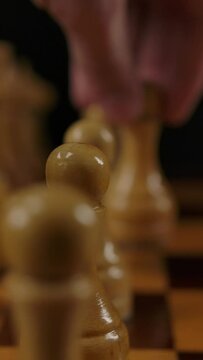 Human's hand makes first move by white pawn e2 e4 in chess game. Macro parallel dolly shot of wooden authentic chess. Two players gaming. Vertical shot.