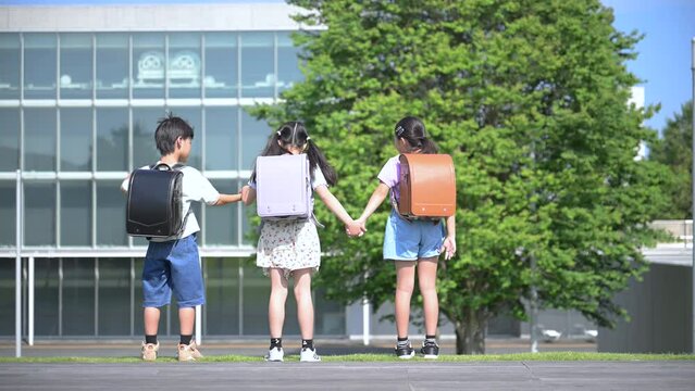 校舎の前でランドセルを背負った小学生たちの後ろ姿顔無し　手を挙げるバンザイの全身のスロー動画