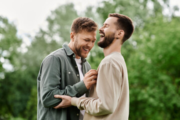 Fototapeta premium A bearded LGBTQ couple shares a laugh while enjoying a sunny day in a green park.