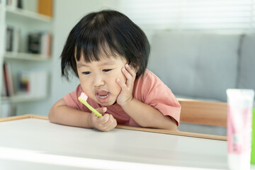 little asian girl presses hand to cheek, suffers from pain in tooth. Teeth decay, dental problems, child emotions and facial expression, oral health care, reducing sweets, fluorine coating