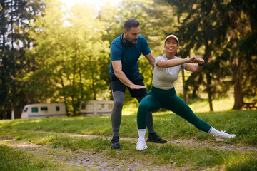 Athletic man assisting his girlfriend with warm up exercises in park.