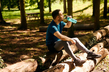 Thirsty athlete drinking water while exercising in nature.