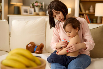 Worried mother using thermometer while checking baby's temperature at home