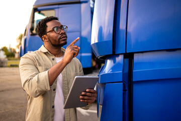 Professional driver standing by truck vehicle and holding tablet computer.
