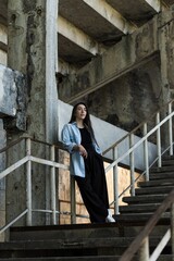 Attractive Caucasian young woman brunette hippie in casual clothes posing on the grounds of an abandoned building while walking on a warm spring day. Style, Fashion, Freedom.