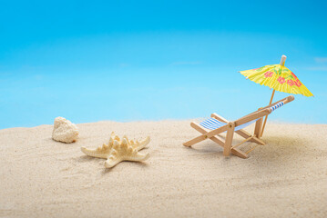 Summer background with sea sand, cocktail umbrella, starfish and beach chair. Space for text.