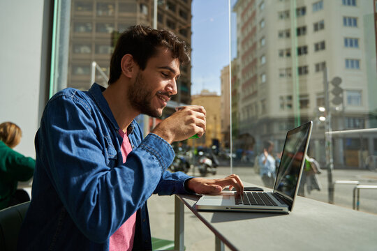 Handsome bearded hipster man use and looking at laptop computer with coffee at table in cafe. Communication and technology concept