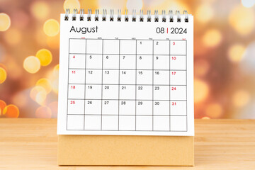 August 2024 desk calendar on wooden table with gold light bokeh background.