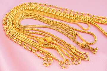 Many gold necklaces on pink velvet cloth.