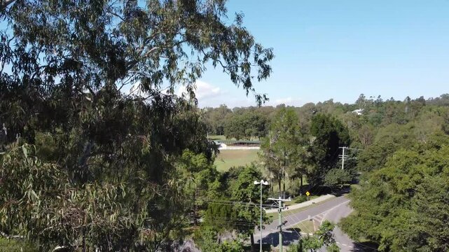 Drone ascending showing a large tree and a roundabout with light traffic and a country Showgrounds in Australia
