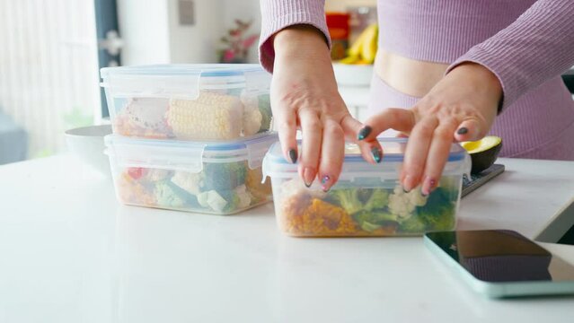 Close up of woman wearing fitness clothing at home in kitchen making up batch of healthy meals for freezer in plastic containers - shot in slow motion