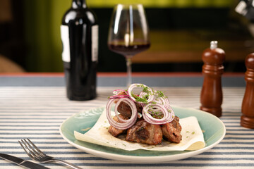 Pieces of meat a grill on white plate against a dark background with wine glass. Shish kebab grill.