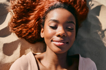 Relaxed young african black woman lying on the sand of the beach with her eyes closed. Close-up of the face